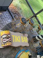 Outdoor decor pieces on pool deck including tiki bar sign, solar lanterns, bird decorations laid out on stone surface near screened patio.