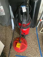 Red and black 1750 PSI electric power washer unit with hose coiled around it and included spray lance. Positioned on a garage floor.