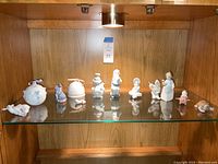Wide view of the collection on wood and glass shelving showing all porcelain Lladro items including figures and decorative bells