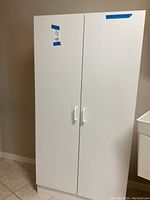 Front view of closed white storage cabinet with two doors and white handles.