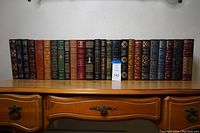 Full front view of 25 leather-bound books arranged side by side on wooden table