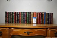 Front view of all 26 volumes on wooden desk, assorted colors.