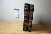 Two signed limited edition books standing upright on a wooden surface showing spine sides with gold embossing and titles.