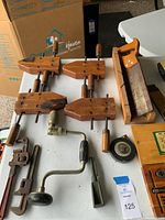 Photo showing wooden bar clamps, adjustable pipe wrench, hand drill, and tape measure on a table