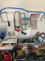 Overview of assorted hand tools hanging on pegboard and some hardware containers on table surface.