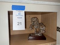 Crystal carousel horse on wooden display base inside wooden cabinet shelf, with auction label 21 visible.