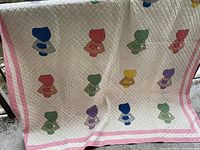 Full view of white quilt with pink borders and colorful Sun Bonnet Sue appliqué figures arranged in multiple rows and columns.