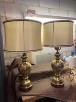 Pair of two vintage frosted gold hand painted floral table lamps on a surface below fluorescent light in garage or basement.