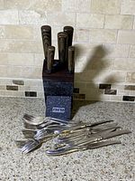 Front view of Hobo Chef knife block with knives inserted and flatware including knives and forks laid out on countertop.