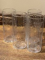 Four clear Finnish highball tumblers with raised bubble pattern arranged in a semi-circle on a wooden surface.