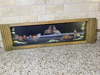 Framed horizontal artwork showing hand painted cockfighting scene with real feathers on display on the floor against stone tile wall.