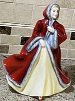 Side view of Royal Doulton Rachel figurine wearing red cloak and cream dress, showing detailed painting and colors.