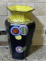 Front angle of hexagonal black matte vase with colorful round geometric shapes and yellow interior rim.
