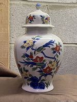 Front view of vintage Asian ginger jar vase displaying hand painted bird and floral decoration on white ceramic surface, lid visible.