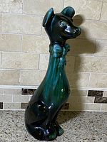 Side view of the long-neck dog figurine showing green and black glaze, bowtie, and hat details