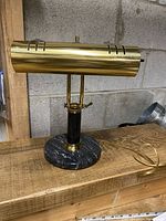 Full view of the vintage brass and black marble bankers piano desk lamp showing the brass shade, pedestal, and marble base on a wooden surface.