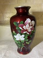 Front side of vintage copper cloisonne vase showing red background and painted white and pink roses with green leaves.