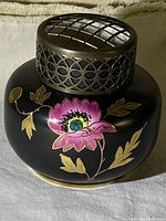 Black ceramic vase with a round shape and wide body featuring a hand painted pink poppy with gold leaves and an antiqued metal lattice flower frog top.