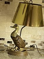 Lamp showing brass shade, brass duck base on a kitchen countertop with tiled backsplash.