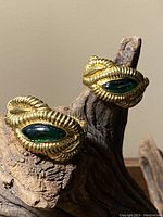 Pair of gold-tone metal earrings with green teardrop-shaped accents displayed on wood.