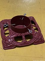 Top side view of the vintage red cast iron tree stand showing the ornate decorative pattern and securing eye bolts.