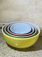 Five vintage Pyrex mixing bowls nested inside each other on countertop, displaying yellow, green, red, blue colors.