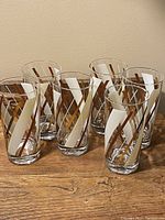Six vintage retro highball tumbler glasses arranged in a triangular formation on a wooden surface, displaying the cream and gold diagonal stripes design.