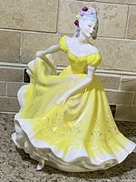 Front and side view of Royal Doulton Ninette figurine showing face, yellow dress with floral details.