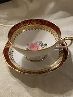 Teacup placed inside matching saucer showing ruby red and gold pattern along rims, floral detail inside teacup, gold rim and handle