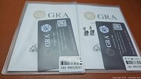 Two certified moissanite stud earrings displayed with their certification cards.