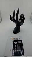 Full view of ring on black display hand with GRA certification card visible