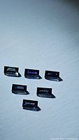 Six rectangular baguette cut blue sapphires arranged on white background showing size and color