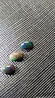 Three oval black opal cabochon stones on textured black fabric showing rainbow iridescence under light.