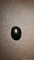 Top-down view of a polished oval cabochon black star sapphire with visible 6-ray star effect on a textured surface.