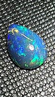 Close-up of pear-shaped Ethiopian black opal cabochon showing brilliant green and blue play-of-color on dark background.