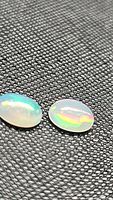 Close-up photo of two oval cabochon Ethiopian opals on textured black surface showing multiple colors and flashes under light.