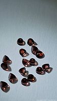 Multiple bullet cut almandine garnet gemstones scattered on white surface under daylight, showing transparent orange-pink hues and high clarity