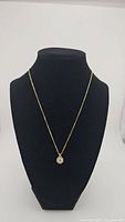 Full view of gold electroplated chain with round moissanite pendant on black display bust.