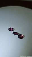 Three natural pink-purple Mulawai garnet gemstones on a plain background, displaying their color and clarity.