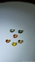 Six loose round brilliant cut rainbow sapphires displayed on white background showing various colors.