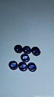 Seven deep royal blue round cabochon sapphires on a white background, showing color and surface shine.