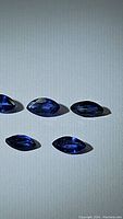Five marquis cut blue sapphire gemstones laid out with visible faceting and rich royal blue color.