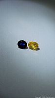 Pair of natural oval cut sapphires; one royal blue and one lemon yellow on white background.