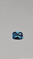 Close-up photo of an 8x6 mm rectangular cushion cut blue topaz gemstone with bright lagoon blue coloration and sharp facets.