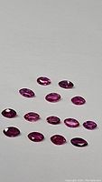 Top-down photo showing 16 small marquis cut rubies with pink to purple tones arranged on white background.
