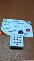 Set of nine round rubies in white display box with certification card from Chanthaburi Gemological Laboratory visible behind