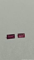 Pair of rectangular baguette cut rubies displayed on a neutral background. Both stones are pink red in color with clean facets and good transparency.