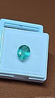 Oval green faceted gemstone in white display box, top view