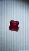 Close-up photo of a square cut red ruby gemstone showing color and clarity details.