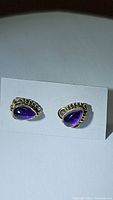 Front view of a pair of teardrop-shaped deep purple amethyst earrings set in sterling silver with beaded decorative edges on a white card